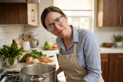 Femme portant des lunettes embuées par la vapeur d'une casserole en cuisinant dans une cuisine moderne